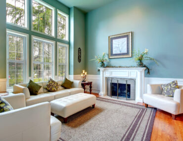 High ceiling aqua living room with white leather couch, ottaman, armchairs and fireplace