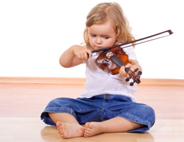 Little girl sitting on the floor struggling with her violin - isolated